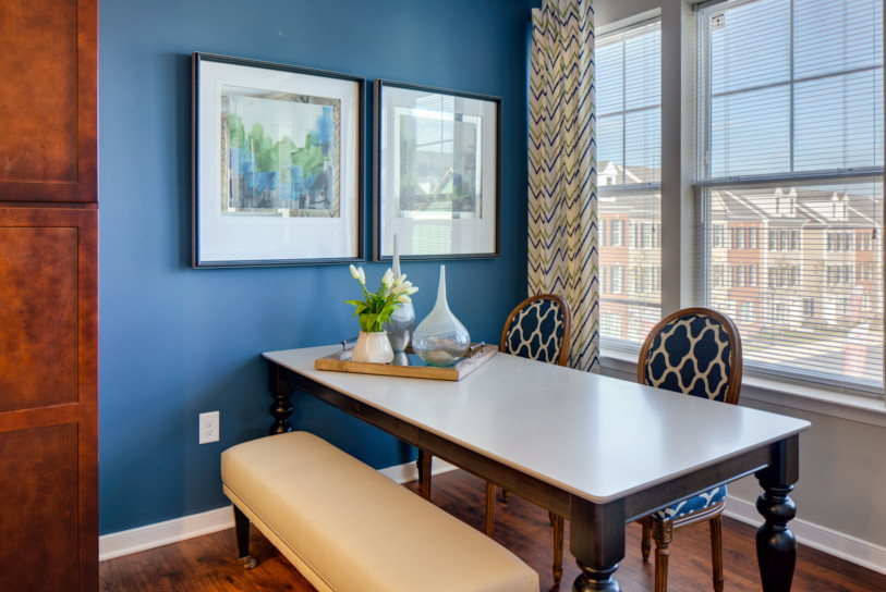 Dining room at Enclave at Box Hill, with blue walls, paintings, a white table, & a refreshing view of other apartments.